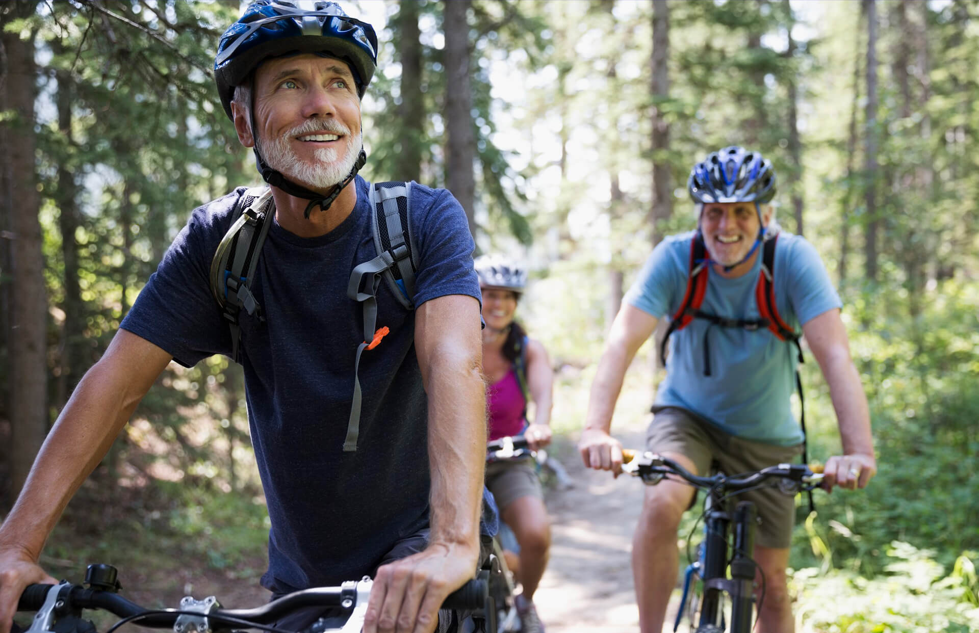 3 people in helmets riding their bikes through a forest trail 